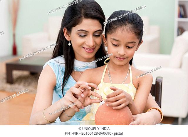 Woman and her daughter inserting a coin into a piggy bank