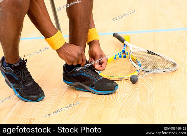 Squash player man preparing for game on court. Black man adjusting his training shoes indoors. Sports concept