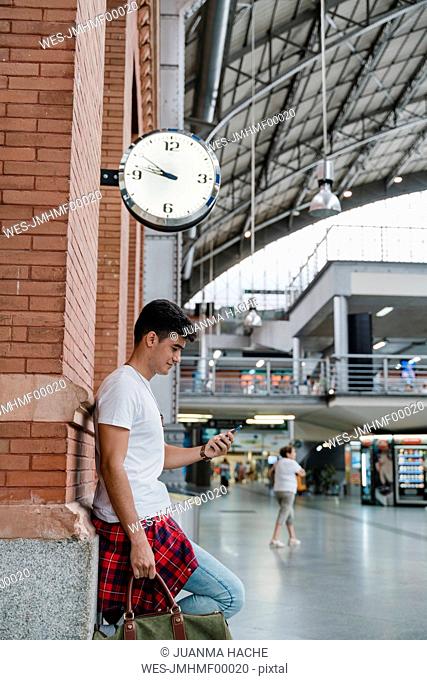 Young man waiting at train station using smartphone