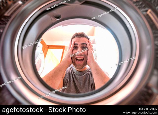 Shocked upset Young man Looking At Stained Bleached Cloth In Washing Machine. View from the inside of washing machine