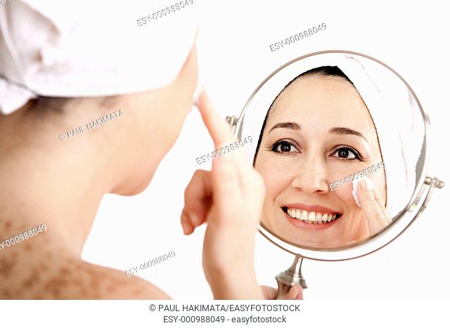 Beautiful happy smiling woman face applying exfoliating cream as anti-aging skincare treatment while looking at mirror, isolated