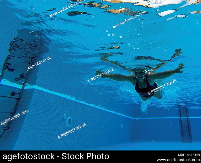 one mature woman or senior swimming alone in a swimming pool and training to be healthy and fitness - active female - under water view