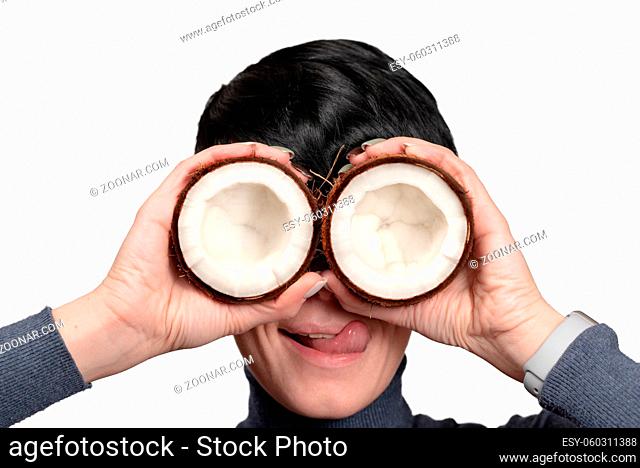 Young woman holding two half of coconut in front of eyes isolated on white background