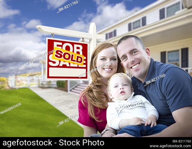Happy young military family in front of sold real estate sign and new house