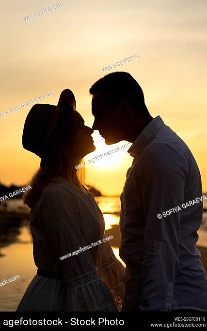 Girlfriend rubbing nose with boyfriend at beach on sunset