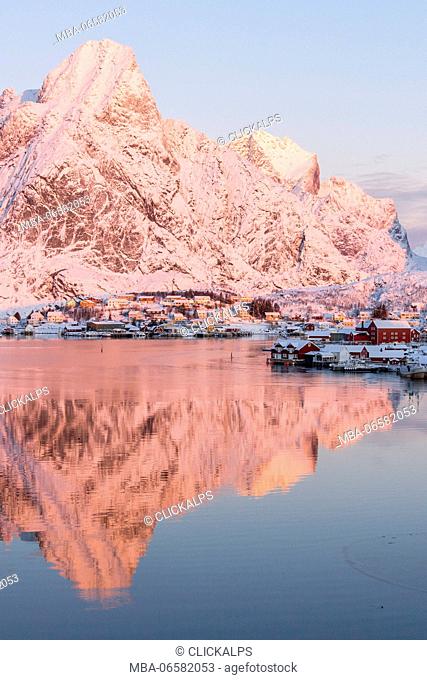 Pink sunrise and snowy peaks frame the frozen sea and the fishing village Reine Bay Nordland Lofoten Islands Norway Europe