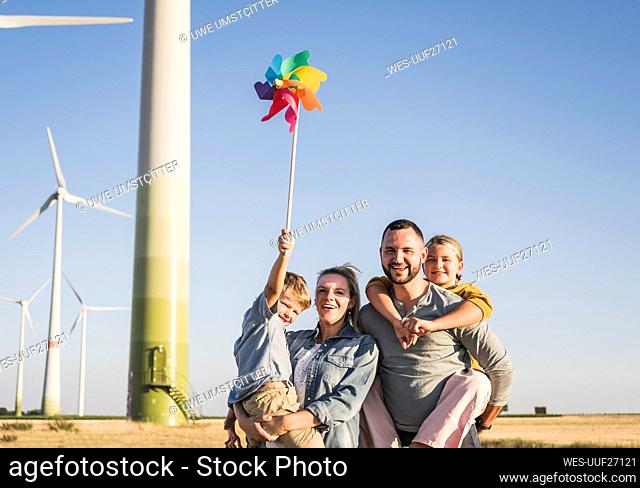 Optimistic family standing in wind park son carrying colorful pinwheel