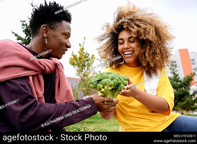 Young man giving broccoli to friend in park