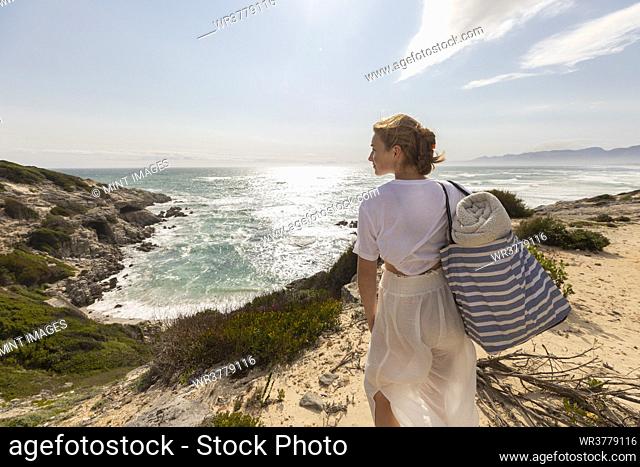 Teenage girl standing on top of a cliff looking over the coastline and inlet