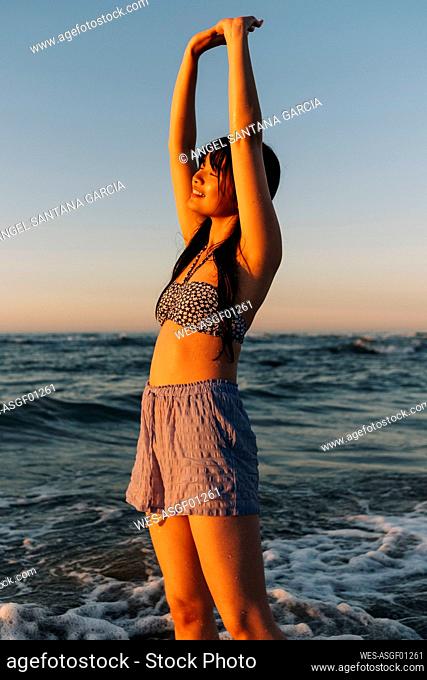 Smiling young woman with arms raised standing at beach