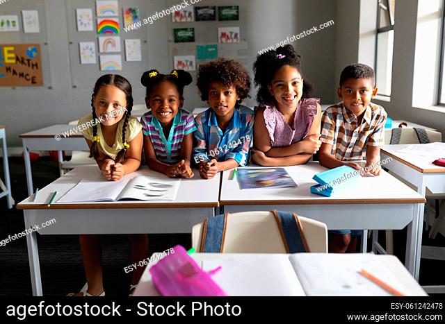 Smiling multiracial elementary school students sitting at desk in classroom
