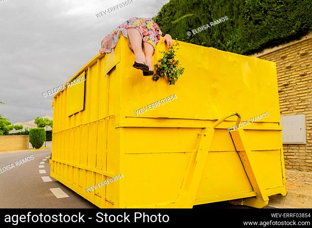 Woman lying on top of yellow container, holding buch of flowers