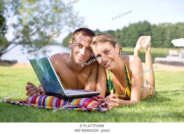 Couple lying on grass using laptop