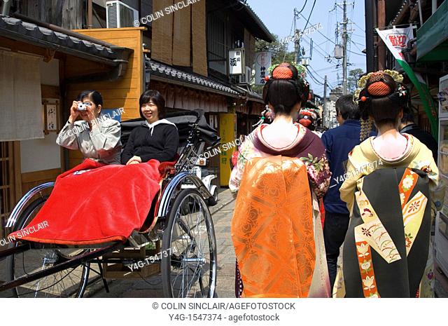 Two geisha walking away from camera in narrow street Gion Kyoto with tourists in rikshaw