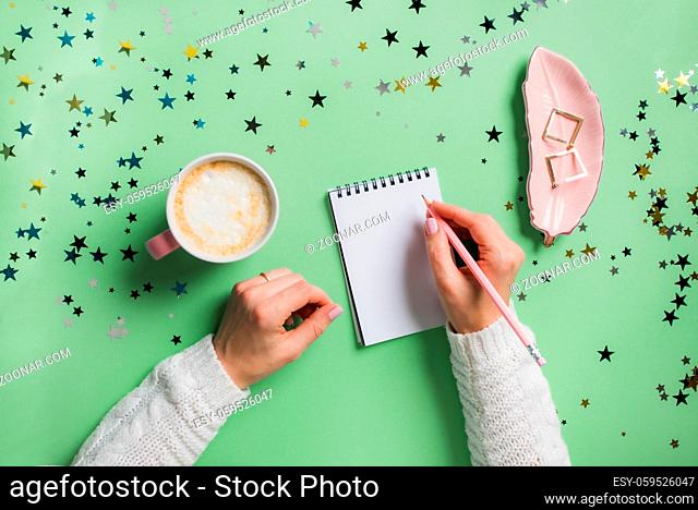 Woman's hands in white sweater making plans for next year, writing them into notebook. Making wish-list or New Year's resolutions concept