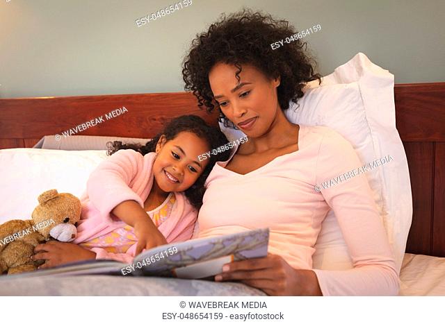 Happy African American mother and her daughter reading a book