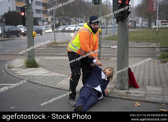 16 November 2022, Berlin: A passerby pulls an activist off the road during a blockade by the environmental protection group ""Last Generation"" on Landsberger...