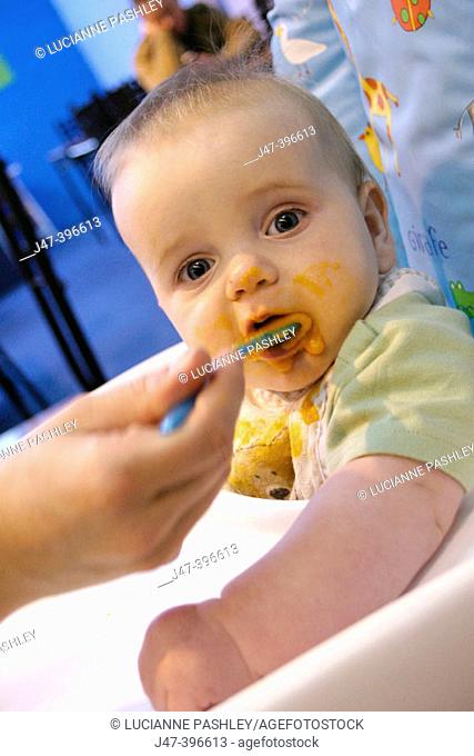 7 month old baby being fed babyfood, in a highchair