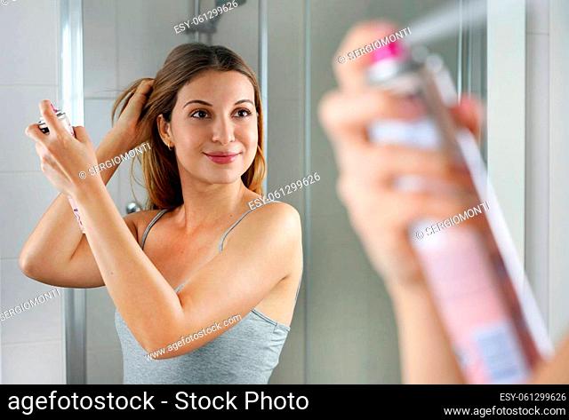 Beautiful young woman applying dry shampoo on her hair. Fast and easy way to keep hair clean with dry shampoo