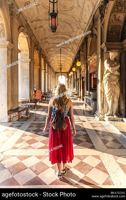 Young woman tourist walking under arcades at St. Mark's Square, Venice, Veneto, Italy, Europe