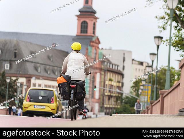 PRODUCTION - 28 August 2023, Hesse, Frankfurt/Main: A cyclist rolls her e-bike across the Old Bridge with a view of the Church of the Teutonic Order