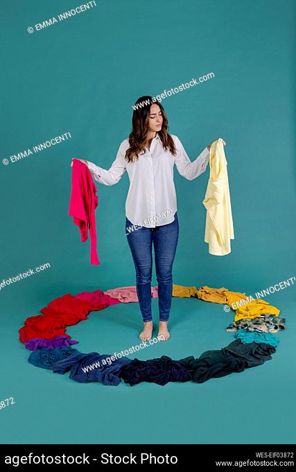 Young woman choosing t-shirts standing against blue background