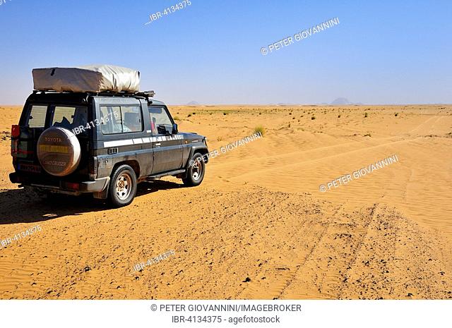 All-terrain vehicle with a roof tent on the dirt track, Aicha monolith behind, Adrar region, Mauritania