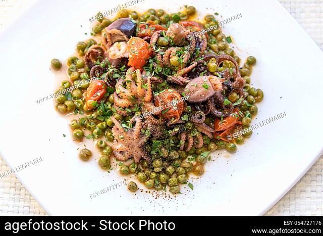Small octopuses cooked with cherry tomatoes, oil and peas. Tasty dish of Italian cuisine served on white plate
