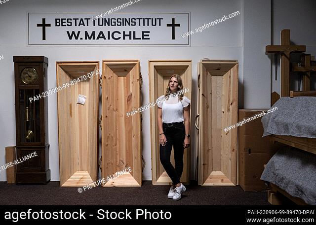 PRODUCTION - 16 August 2023, Baden-Württemberg, Geislingen an der Steige: Mortician Emily Maichle stands in front of coffins in a warehouse of the family...