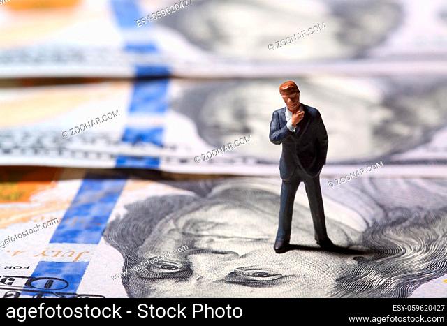 Miniature figurine businessman with 100 dollars banknote on background. Concept