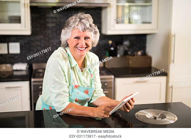 Portrait of smiling senior woman using digital tablet on counter in kitchen