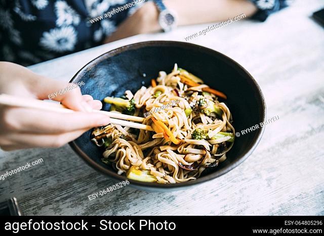 Woman eating asian noodles udon with pork in cafe. Asian noodles udon with pork close-up in a bowl on the table