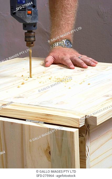 Man drilling a hole in a piece of wooden furniture