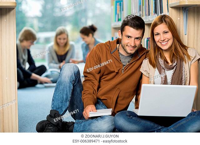 Smiling college students with laptop in library