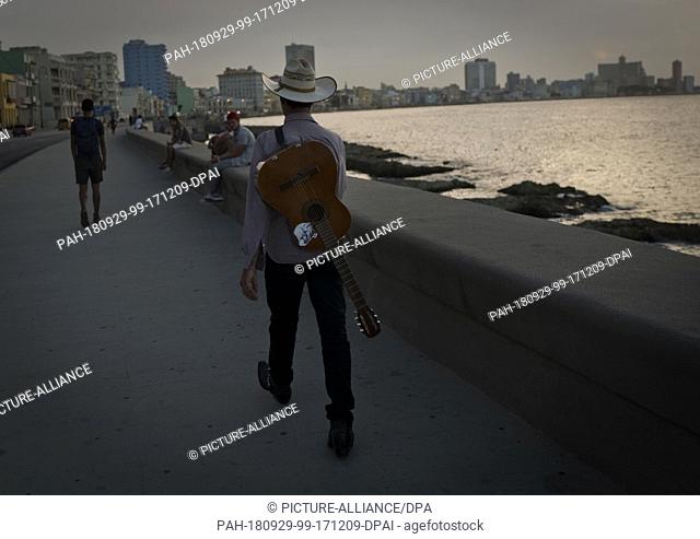 28 September 2018, Cuba, Havanna: A Cuban carries his guitar on his back and sets off in search of tourists at the Malecon. Photo: Eliana Aponte/dpa