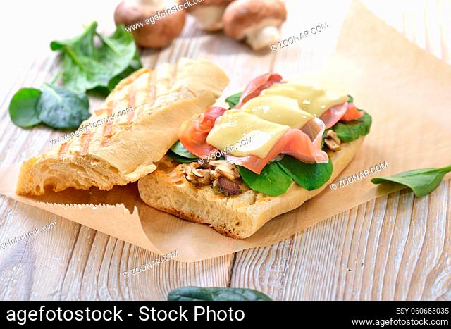 Heißes Sandwich aus dem Grill mit feinem Serrano Schinken, Pilze und jungem Spinat mit Käse überbacken - Street food: Toasted panini with Spanish ham and...