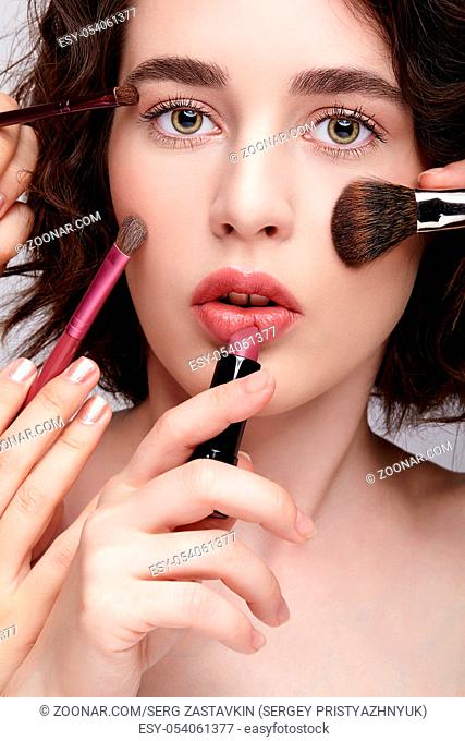 Make-up artist apply beauty makeup on the face of a beautiful girl. Visagist with makeup brush in hand