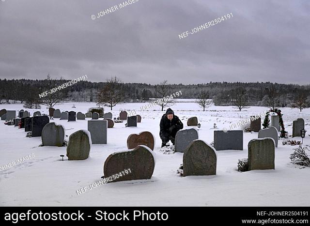 Man crouching by grave at cemetery