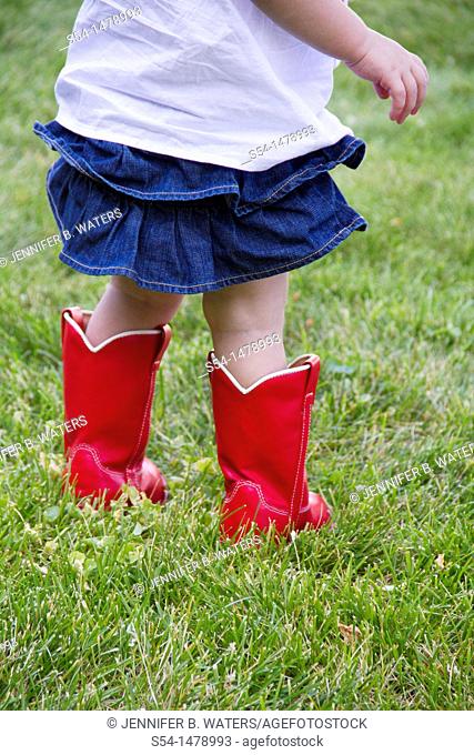 A toddler standing in a lawn wearing bright red boots
