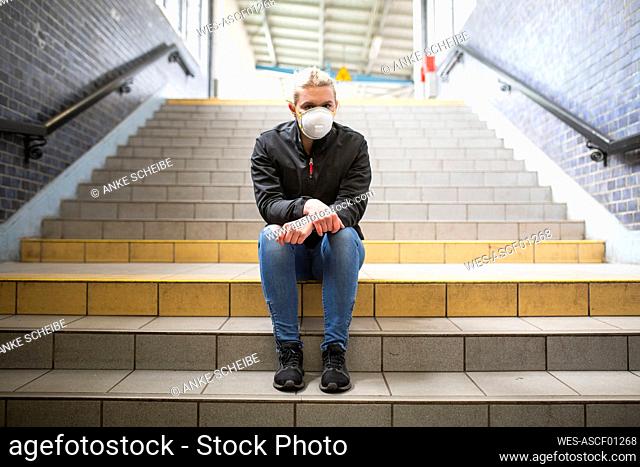 Teenage girl wearing protective mask and gloves sitting on stairs of train station