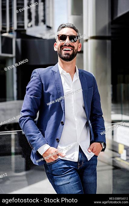 Cheerful businessman with hands in pockets leaning on glass railing