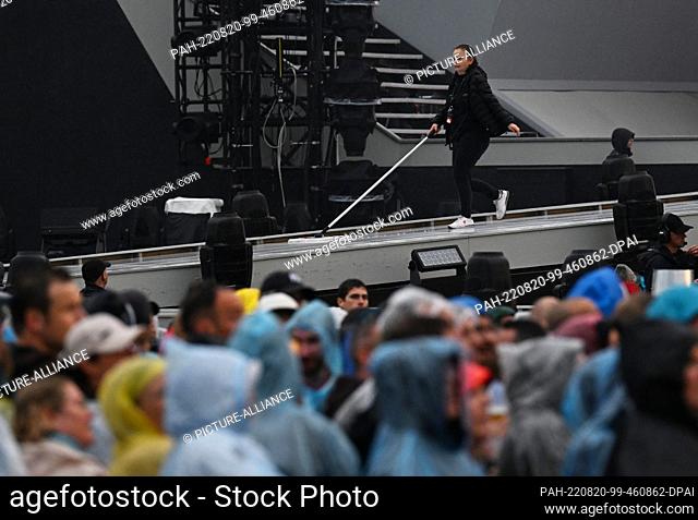 20 August 2022, Bavaria, Munich: Helpers wipe the rainwater off the stage before the start of Helene Fischer's open-air concert at Messe München