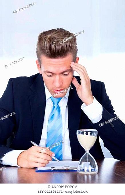 Businessman Filling Form In Front Of Hourglass