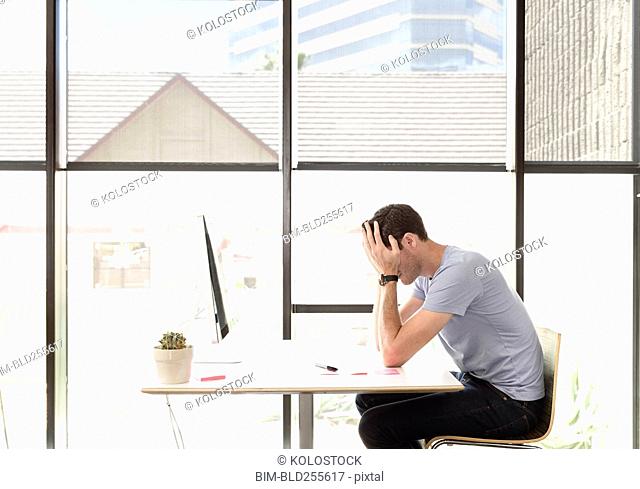 Frustrated Caucasian man with head in hands at desk