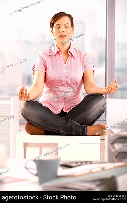 Young businesswoman sitting in lotus posture on office cabinet, meditating