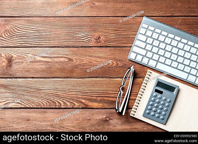Still life of accountant workspace with office accessories. Flat lay wooden desk with computer keyboard, calculator and notepad