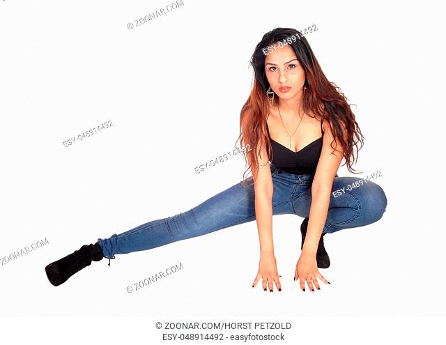A beautiful slim young woman in jeans and a black corset crouching on the floor, looking serious, isolated for white background