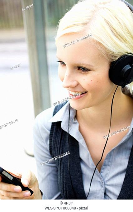 Germany, Bavaria, Munich, Young woman listening music, smiling