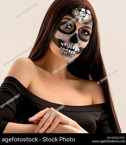 Woman with smart artistic makeup in horror style posing with silver skull in studio in her hands