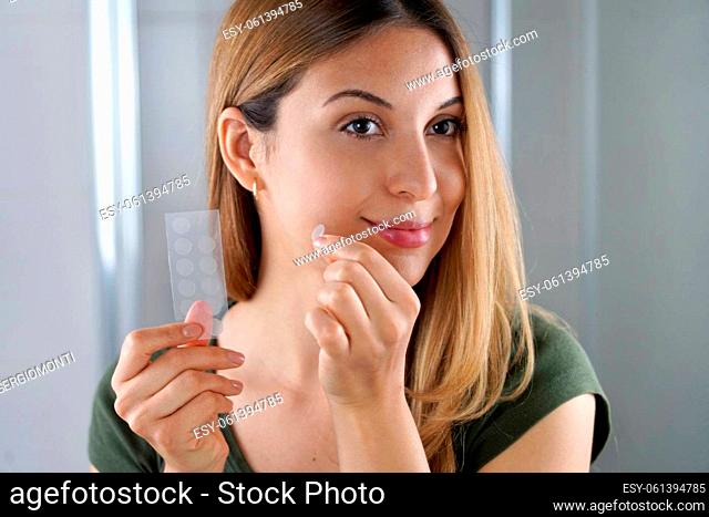 Beautiful young woman applying acne treatment anti-pickel patch on a pimple in bathroom at home